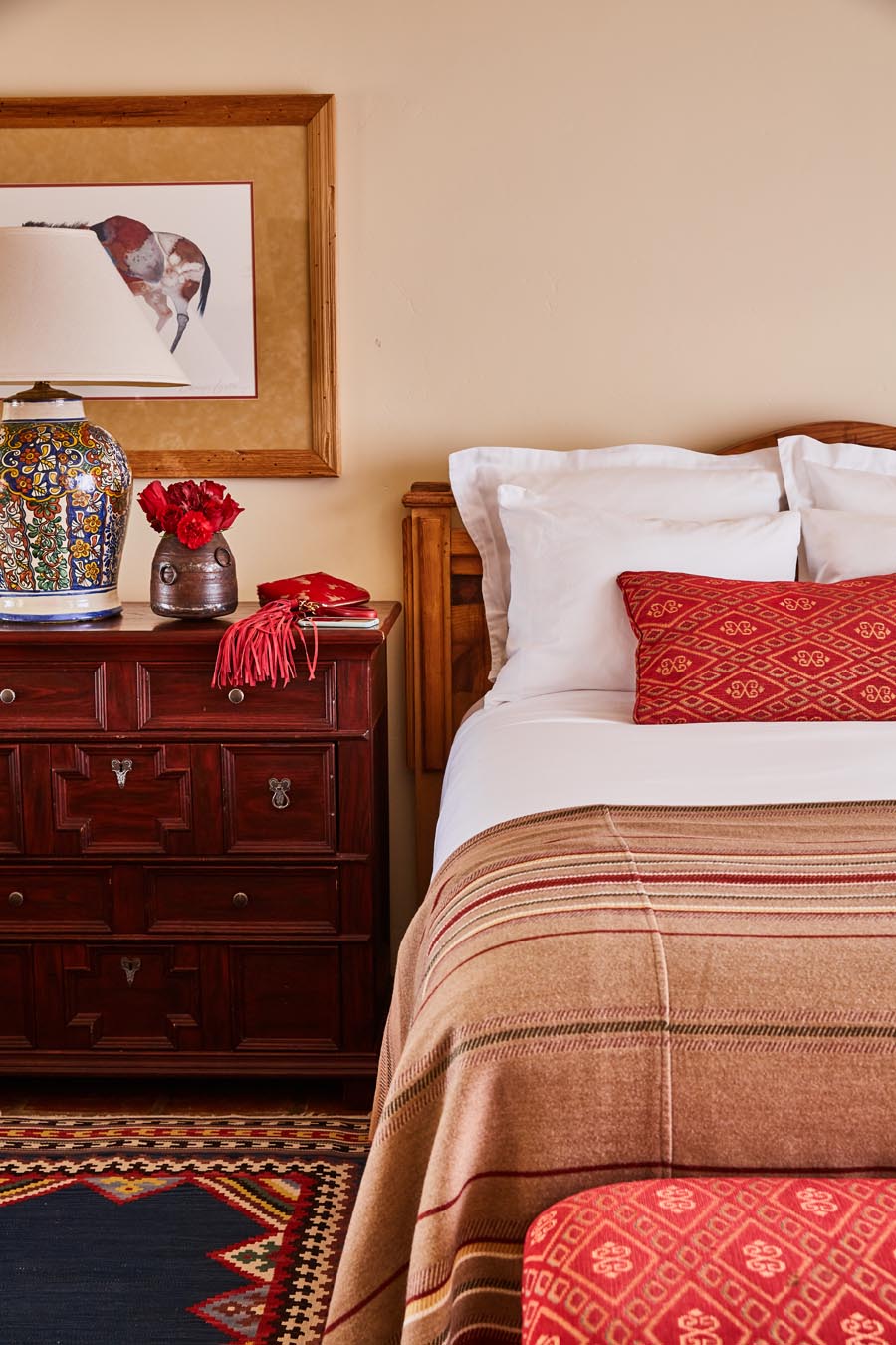 Bed with red pillow beside dresser and lamp